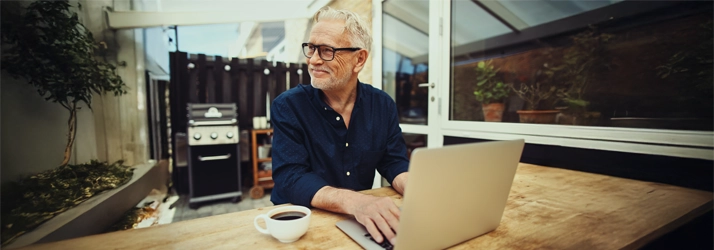 Eye Doctor Sault Ste. Marie MI Smiling Man A man sitting outside smiling. He is wear glasses and typing on a laptop.
